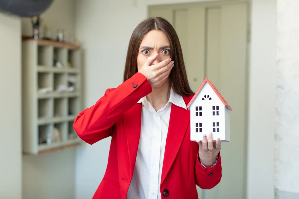 woman holding a home model and covering her face with hand in amazement